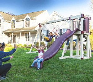 white and maroon playset with swings and a slide in front of a house