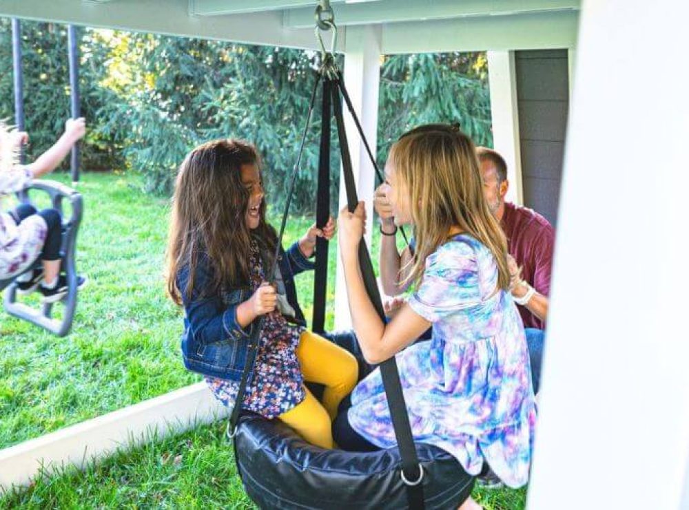 two little girls swinging on a tire swing under a playset