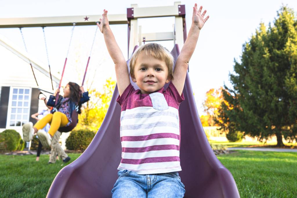 child with arm up going down slide of outside play set